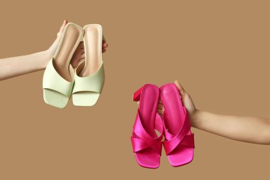 Bej arka planda farklı topuklu sandaletleri olan kadın elleri.