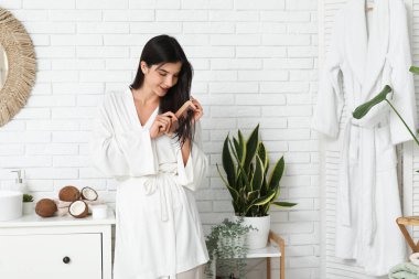 Güzel genç bir kadın banyodaki saçlara hindistan cevizi yağı sürüyor.