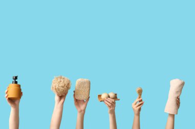 Kozmetik ürünü şişesi, banyo süngeri, tahta masaj topları, mavi arka planda vücut fırçası ve havlusu olan kadın elleri.