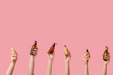 Pembe arka planda kozmetik ürünleri olan kadın elleri