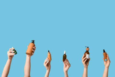 Mavi arka planda farklı kozmetik ürünleri şişeleri olan kadın elleri