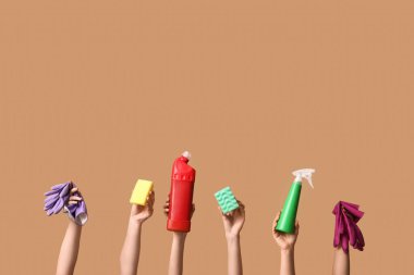 Deterjan şişeleri, süngerler ve kahverengi arka planda lastik eldivenler tutan kadın elleri.