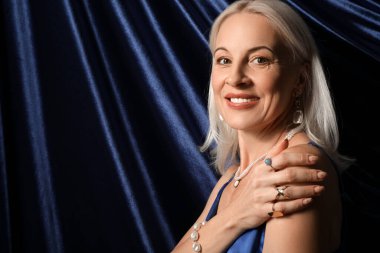 Mavi arka planda güzel mücevherler içinde mutlu olgun bir kadın.