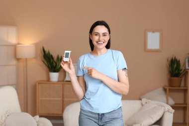 Şeker hastası genç bir kadın odadaki glukometreyi işaret ediyor.