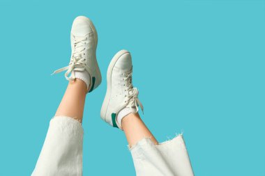 Mavi arka planda beyaz spor ayakkabılı genç bir kadının bacakları.