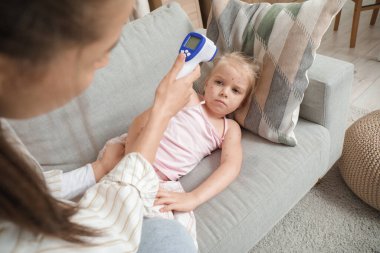 Mother measuring temperature thermometer of her little daughter ill with chickenpox at home clipart