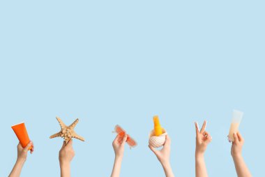 Mavi arka planda deniz yıldızı, güneş gözlüğü ve güneş kremi olan bir sürü el.