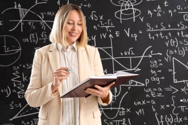 Sınıfta tahtaya yakın not defteri ve kalemi olan olgun bir matematik öğretmeni.
