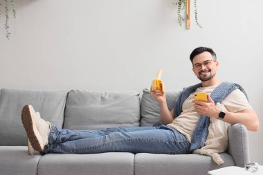 Muzlu genç adam evdeki koltukta cep telefonu kullanıyor.