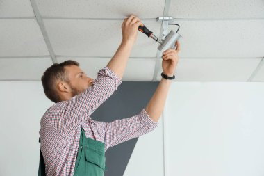 Odanın tavanına alarm sistemi kuran tornavidalı bir erkek işçi.