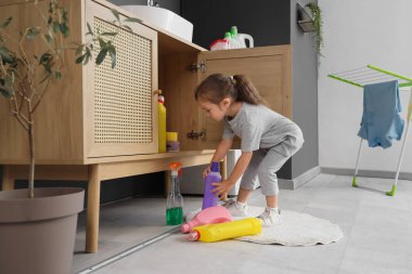 Çamaşır odasındaki açık çekmeceden çıkan deterjan şişeleriyle küçük şirin bir kız. Tehlikedeki çocuk