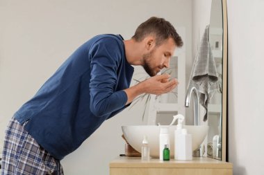 Yakışıklı genç adam evde tıraş yaptıktan sonra sakalını yıkıyor.