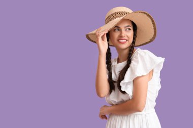 Güzel, genç, mutlu, stil sahibi, hasır şapkalı, mor arka planda örgülü bir kadın.