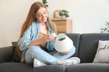 Genç bir kadın evdeki kanepede ampulü lambaya vidaladı.