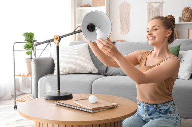 Genç bir kadın evdeki masada ampulü lambaya vidaladı.