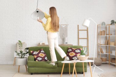 Genç bir kadın evdeki tavan lambasına ampul takıyor.