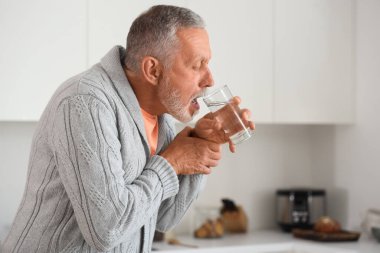 Parkinson sendromundan muzdarip yaşlı adam mutfakta su içiyor.