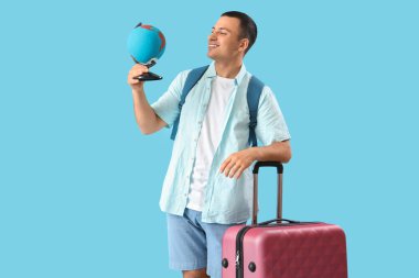 Mavi arka planda çantaları ve küresi olan erkek turist