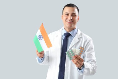 Male doctor with flag of India and pills on grey background. National Doctor's Day celebration clipart