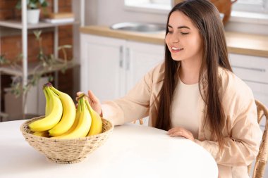 Genç bir kadın mutfaktaki masadan muz alıyor.