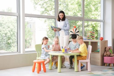 Anaokulundaki masada kitap ve küçük çocuklarla ilgili resim çizen anaokulu öğretmeni.