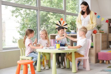 Anaokulunda birbirine beşlik çakan küçük çocuklar ve anaokulu öğretmeni.