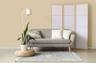 Oturma odasının içinde gri kanepe, bitki ve katlanmış ekran var.