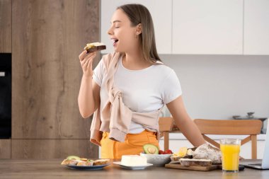 Güzel, genç, mutlu bir kadın elinde bir bardak meyve suyu ve lezzetli bir tost ve evde taze tereyağı tutuyor.