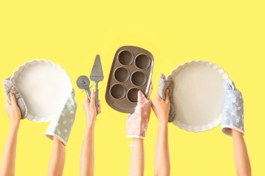 Sarı arka planda farklı pişirme aletleri tutan kadın eller.