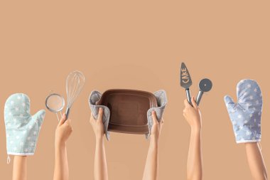 Bej arka planda farklı pişirme aletleri ve eldivenleri olan kadın elleri.