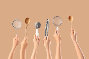 Bej arka planda farklı pişirme aletleri olan kadın elleri