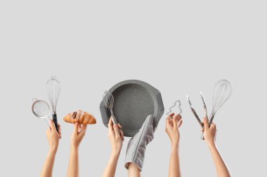 Gri arka planda pişirme aletleri ve lezzetli kruvasanlar tutan kadın eller.