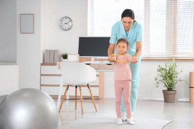 Kadın osteopat ve elastik bantlı küçük bir hasta klinikte egzersiz yapıyor.