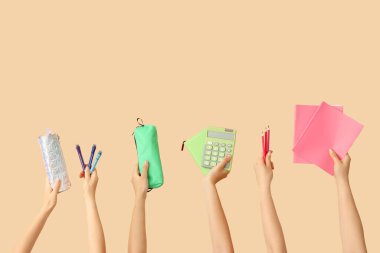 Okul malzemesi ve bej arka planda kalemleri olan kadın eller.