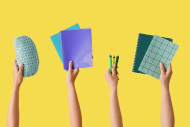 Okul gereçleri ve sarı arka planda keçeli kalemler olan kadın eller.