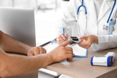 Nabız oksimetresi olan genç bir adam ve klinikte doktor, yakın plan.
