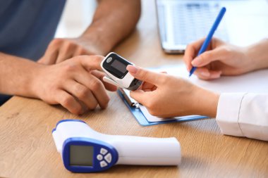 Nabız oksimetresi olan genç bir adam ve klinikte doktor, yakın plan.