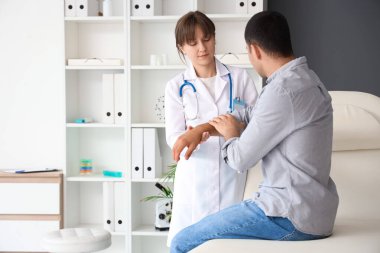 Kadın doktor klinikte erkeğin kolunu muayene ediyor.