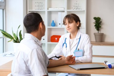 Klinikteki doktorla kan basıncını ölçen genç bir adam.