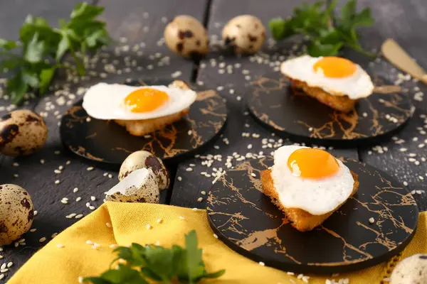 Lezzetli kızarmış bıldırcın yumurtası, tost, maydanoz ve siyah ahşap arka planda susam tohumlu kompozisyon.