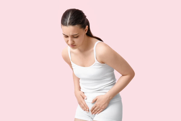Молодая женщина в нижнем белье страдает циститом на розовом фоне