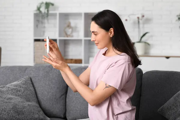 stock image Diabetic young woman using lancet pen on sofa at home