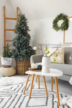 İçinde ağaç dalları olan vazolar ve aydınlık oturma odasındaki sehpanın üzerinde noel süsleri.