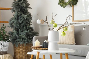 İçinde ağaç dalları olan vazolar ve aydınlık oturma odasındaki sehpanın üzerinde noel süsleri.