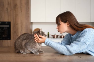 Güzel, genç, mutlu, kedisi olan bir kadın. Mutfakta öpüşüyor.
