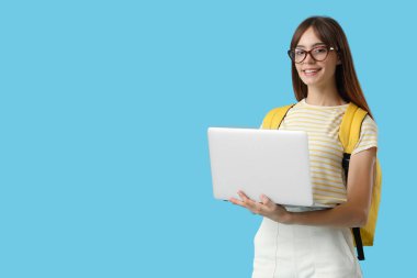 Mavi arka planda dizüstü bilgisayarı ve sırt çantası olan mutlu bir kız öğrenci.