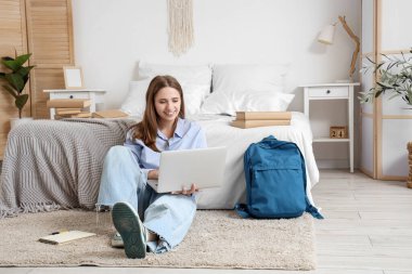 Sırt çantası, kitapları ve dizüstü bilgisayarı olan mutlu kız öğrenci evde ders çalışıyor.