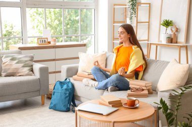 Sırt çantası ve kitaplarıyla evde çalışırken meditasyon yapan mutlu kız öğrenci.