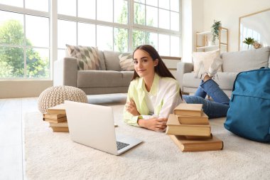 Kitapları, sırt çantası ve dizüstü bilgisayarı olan mutlu kız öğrenci evde ders çalışıyor.