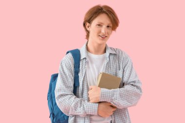 Pembe arka plan kitapları olan kızıl saçlı bir erkek öğrenci.